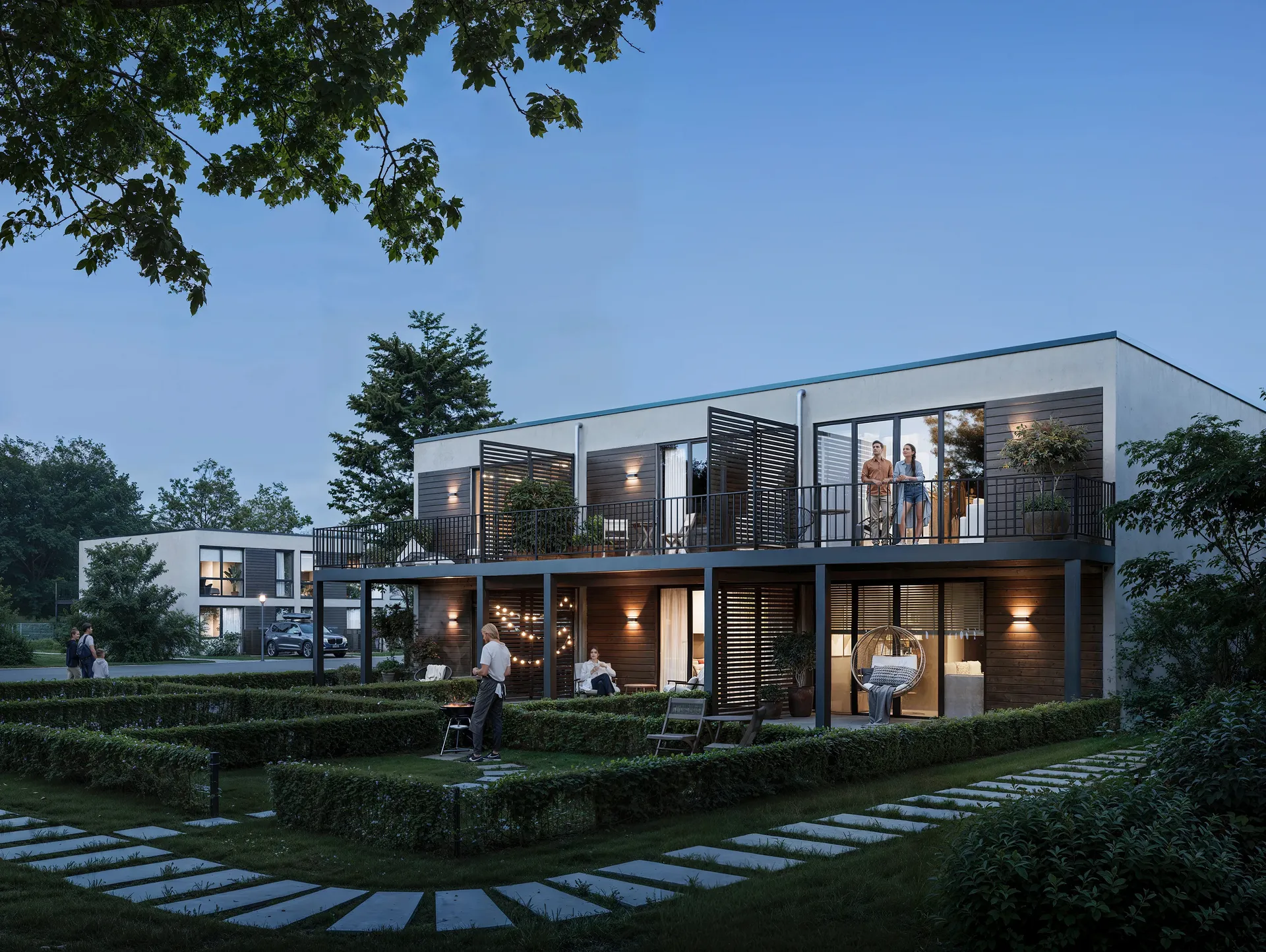 Vue en soirée d'une maison dont les résidents se détendent sur les balcons.
