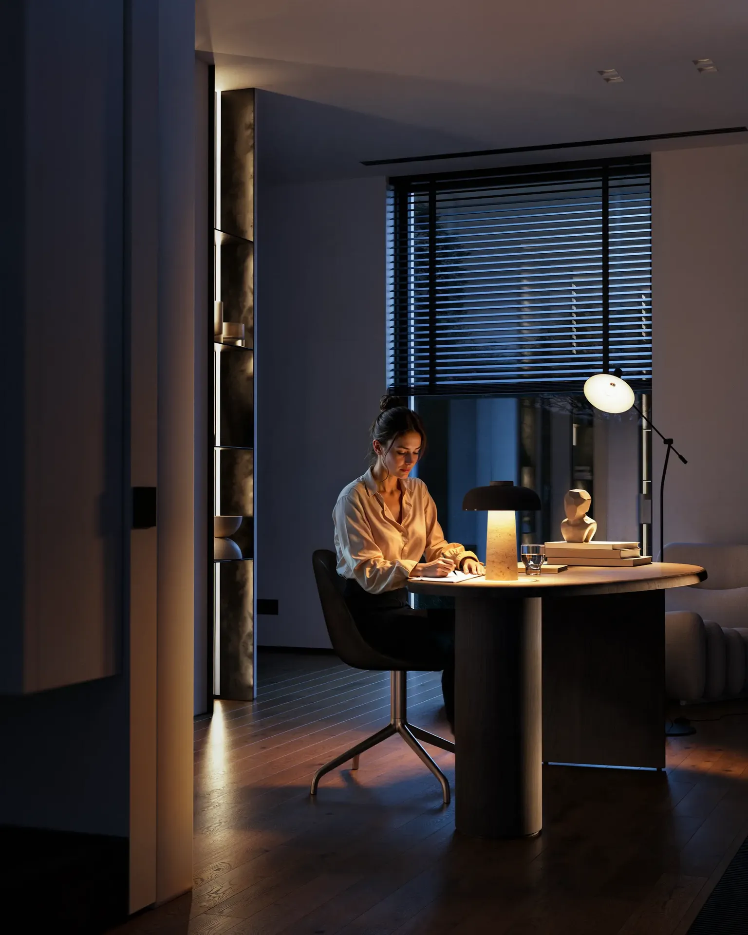 Vue agréable en soirée d'un bureau à domicile, montrant une femme écrivant à un bureau sous une lumière ambiante chaude.