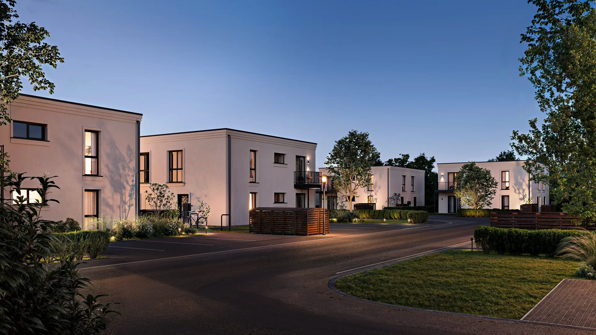 Vue en soirée sur la rue d'un complexe résidentiel avec façades éclairées et aménagement paysager.