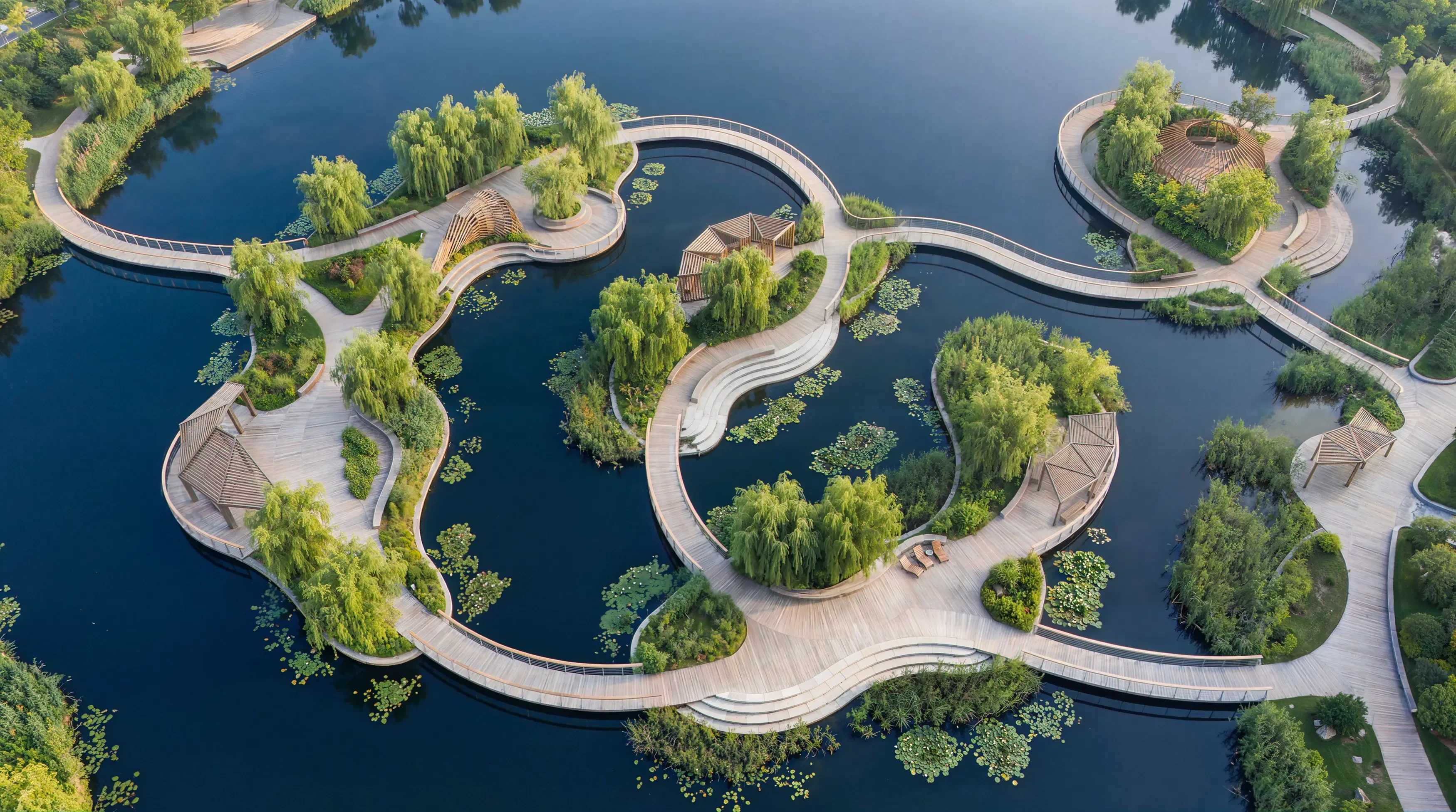 Aerial view of a winding wooden boardwalk over calm water in a park.